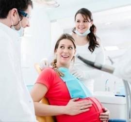Femeie însărcinată zâmbind în timp ce este consultată de un dentist și o asistentă medicală.