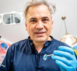 Medic stomatolog cu mănuși albastre, ținând un instrument dentar și un oglindă dentară.