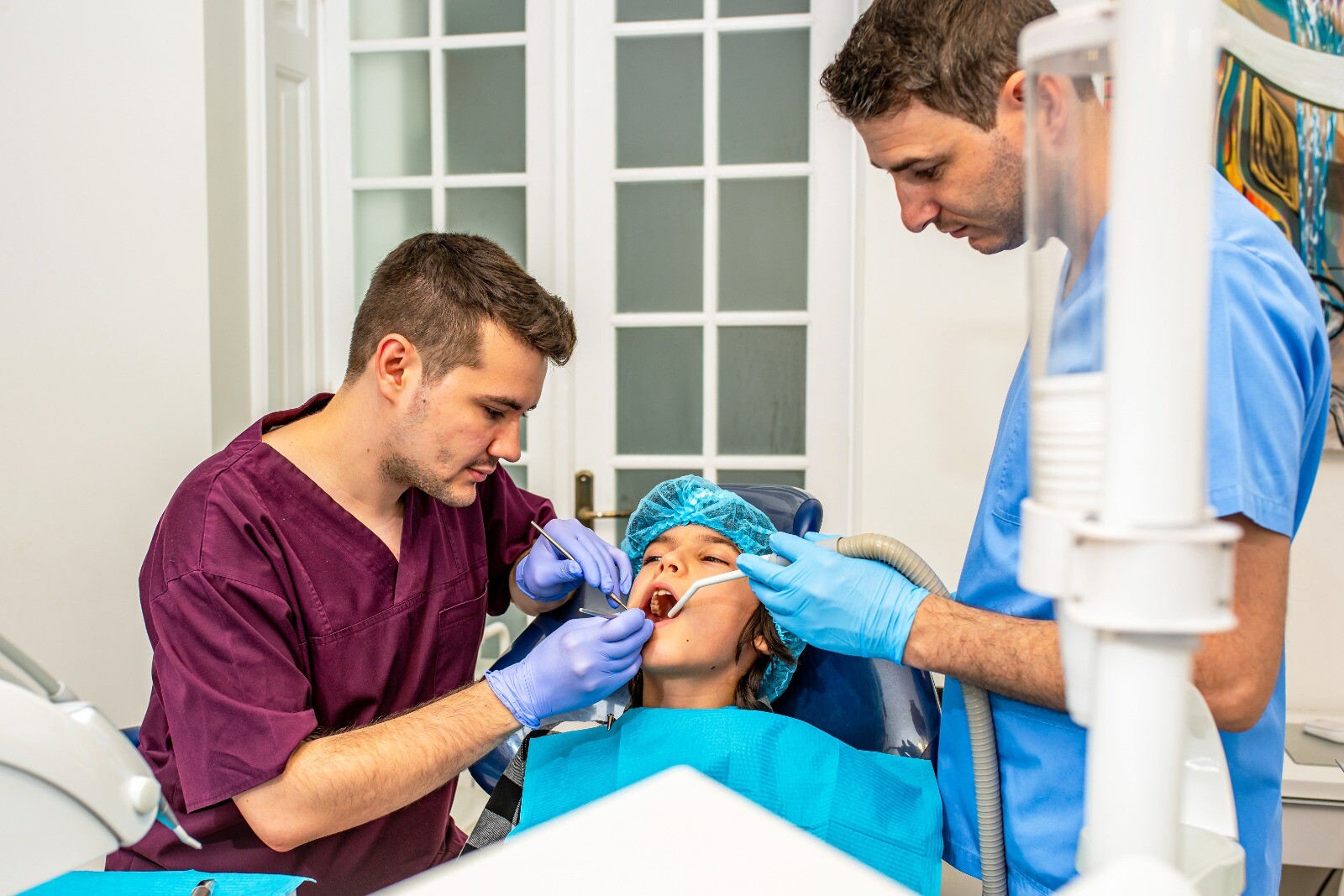 Doi dentiști efectuează o procedură stomatologică asupra unei paciente într-un cabinet dentar.