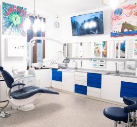 Cabinet stomatologic modern cu scaun de dentist, echipamente și decor colorat pe pereți.