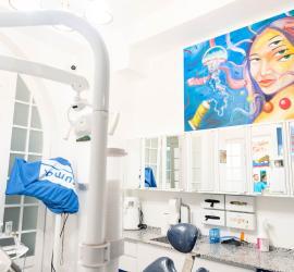 scenă dintr-o clinică stomatologică albă cu mobilier alb, avionul de radiografie și un tablou colorat pe perete; textul menționează Dr. Aristide și București, iar ambianța sugerează un spațiu medical modern