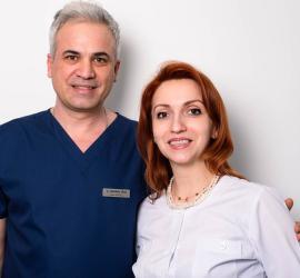 Doi membri ai echipei cabinetului medical: un medic în halat bleu încrezător lângă o femeie cu păr roșu, zâmbind, într-un decor alb, sugerând medici stomatologi Diana Paun