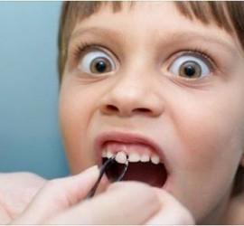 Un copil cu ochii mari, având gura deschisă, în timp ce un dentist folosește un instrument dentar.