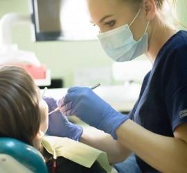 Asistentă dentară cu mănuși și mască examinând un pacient în cabinetul stomatologic.