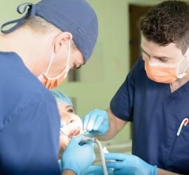 Doi medici stomatologi care examinează un pacient în timpul unei consultații dentare.