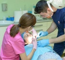 Un medic stomatolog și o asistentă efectuează o intervenție dentară asupra unei paciente.