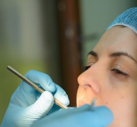 Medic stomatolog examinând dinții unei paciente cu un instrument dentar.