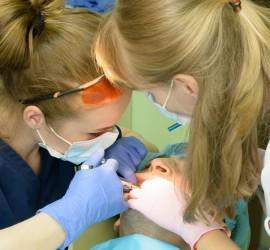 Două asistente dentare efectuează o procedură pe un pacient în cabinetul stomatologic.