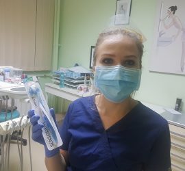 Periuță de dinți Sensodyne ținută de o persoană în uniformă medicală, cu mască și vizieră.