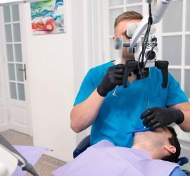 Medic dentist folosind un microscop dentar pentru a efectua un tratament asupra unui pacient în cabinet.