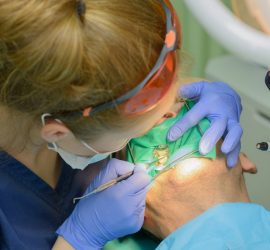 Medic stomatolog efectuează o intervenție dentară pe un pacient cu mască de protecție.