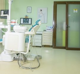 Un scaun stomatologic alb și echipamente într-un cabinet stomatologic cu pereți verzi.