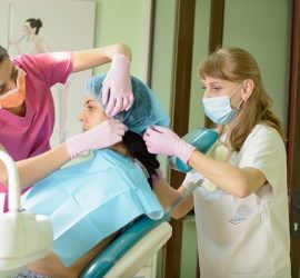 Două asistente medicale pregătesc o pacientă pentru un tratament dentar într-un cabinet stomatologic.