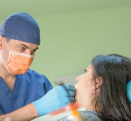 Medic stomatolog cu mască și mănuși examinând un pacient pe scaunul stomatologic.