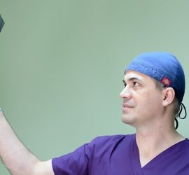 Medic purtând un halat și mănuși, examinând o radiografie cu atenție.