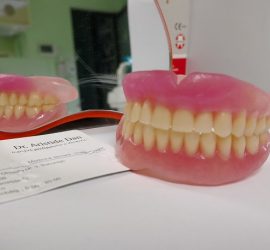 Proteză dentară cu dinți artificiali în fața unei oglinzi și a unei cărți de vizită.