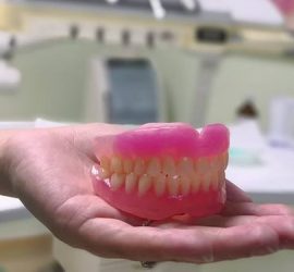 Model de dinți artificiali, prezentat pe o palmă, cu detalii clare ale dinților și gingiilor.