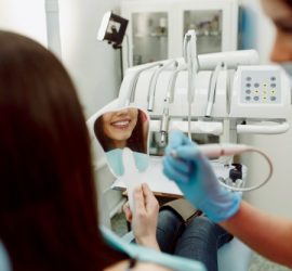 Pacientă zâmbind în oglindă în timp ce un dentist lucrează la tratamentul dentar.
