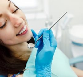 Femeie zâmbitoare la dentist, ținând un instrument de examinare dentară în mână.