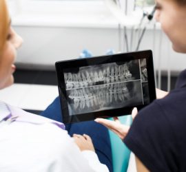 O radiografie dentară afișată pe o tabletă, vizualizată de două persoane într-un cabinet stomatologic.
