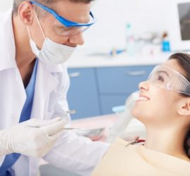 Un dentist îmbrăcat în halat alb examinează o pacientă în cabinet stomatologic.