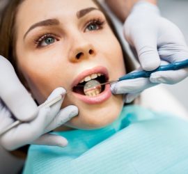 Femeie cu gura deschisă în timpul unei consultații dentare, cu instrumente dentare în mână.