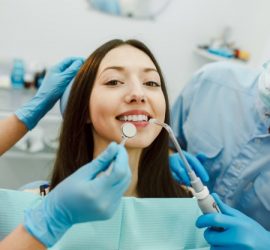 Tânără femeie zâmbind în timp ce un dentist o examinează cu un instrument dentar.