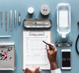 Un set de instrumente medicale, un program de raportare și un telefon pe o masă de lucru.