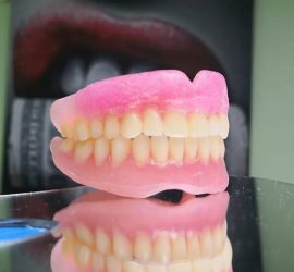 Proteză dentară roz cu dinți artificiali pe un suport reflectorizant.