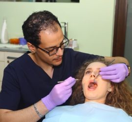 Un dentist examinează o pacientă în timp ce folosește un instrument dentar.