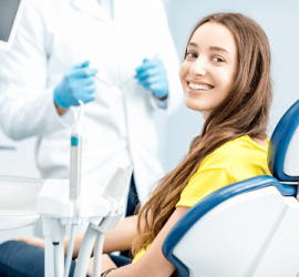 Tânără cu părul lung și zâmbet larg, așezată pe un scaun de dentist, în cabinet stomatologic.