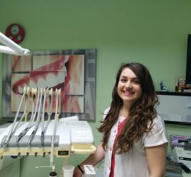 Asistent medical zâmbind în fața unui echipament stomatologic într-un cabinet.