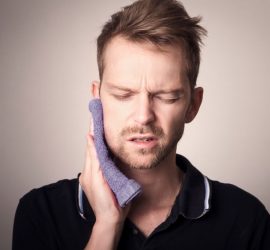 Bărbat cu un prosop pe obraz, arătând semne de disconfort dentar.
