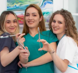Trei femei imbracate in ținută medicală pozează zâmbind cu intrumente medicale în mână, în cabinetul stomatologic