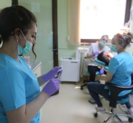 Asistentă medicală îmbrăcată în uniformă, utilizând un telefon mobil într-un cabinet stomatologic.