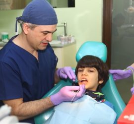 Medic stomatolog cu halat și bonetă examinând un copil în cabinetul stomatologic.
