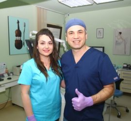 Două persoane în uniformă medicală zâmbind într-o clinică, una dintre ele arătând cu degetul mare în sus.