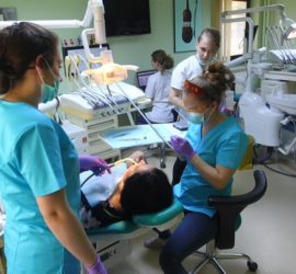 Două asistente medicale efectuează o consultație dentară pentru un pacient într-un cabinet stomatologic.