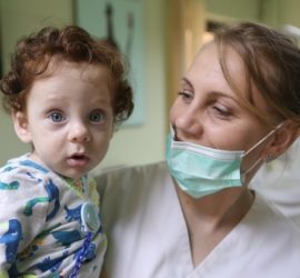 Medic stomatolog ținând un copil în brațe, amândoi având expresii neutre.