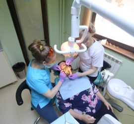 Două asistente stomatologice efectuează o procedură pe un pacient într-un cabinet stomatologic.