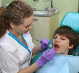 Dentist using a dental mirror to examine a child's teeth in a dental clinic.