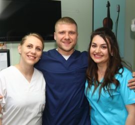 Trei membri ai echipei medicale zâmbind, purtând uniforme de diferite culori.