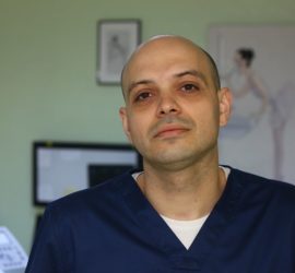 Medic stomatolog cu părul scurt, îmbrăcat în uniformă albastră, privind spre cameră.