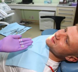 Un pacient zâmbind în timp ce un dentist îi arată un set de instrumente dentare.