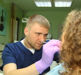 Dentist in blue scrubs examining a patient's teeth with a dental tool.