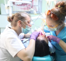 Două asistente dentare efectuează o procedură stomatologică pe un pacient într-un cabinet stomatologic.