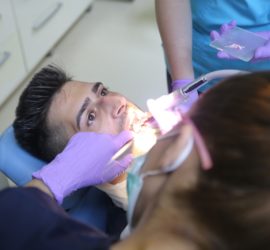 Un pacient cu gura deschisă în timpul unei consultații stomatologice, cu un medic stomatolog care lucrează.