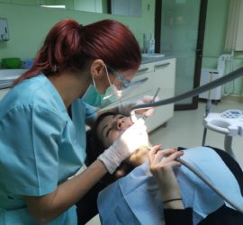 Asistentă stomatologică care lucrează la un pacient în timpul unui tratament dentar într-un cabinet stomatologic.