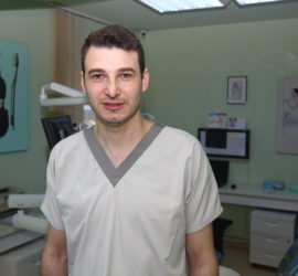 Medic stomatolog îmbrăcat în uniformă, zâmbind în cabinetul stomatologic.