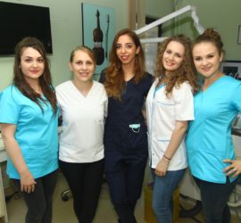 Cinci medici dentiști pozând împreună într-un cabinet stomatologic.